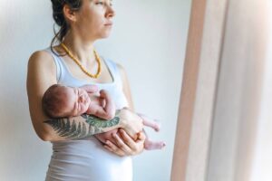 Junge Mutter hält Baby im Arm und guckt nachdenklich.